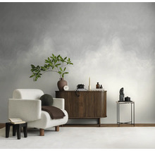 Vliesbehang met kleurverloop in wolkenlook in een lichte, modern ingerichte woonkamer met een witte fauteuil en een houten dressoir.