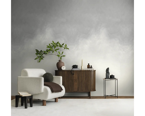 Vliesbehang met kleurverloop in wolkenlook in een lichte, modern ingerichte woonkamer met een witte fauteuil en een houten dressoir.