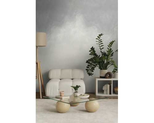 Moderne woonkamer met modulaire fauteuil, glazen salontafel op bolvormige poten, houten driepoot vloerlamp en getextureerd behang.