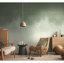 Woonkamer met abstract behang in groen en wit, rotan stoel, houten dressoir en een hanglamp.