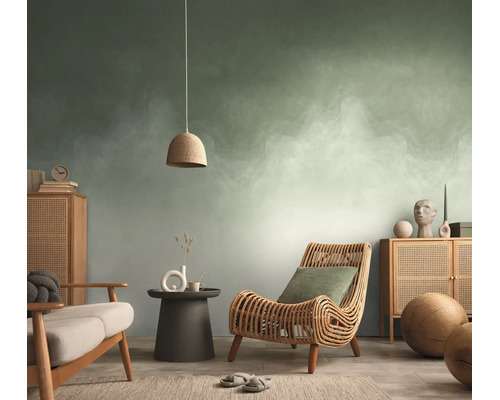 Woonkamer met abstract behang in groen en wit, rotan stoel, houten dressoir en een hanglamp.