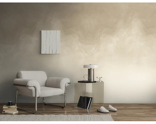 Moderne woonkamer met gestructureerd wandontwerp in beige, grijze fauteuil met chromen frame, transparante bijzettafel en parketvloer.