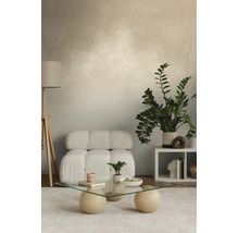 Moderne woonkamer met wandstructuur, witte fauteuil, glazen salontafel met bolvormige poten, houten vloerlamp en grote groene plant.