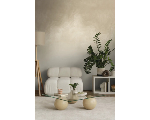 Moderne woonkamer met wandstructuur, witte fauteuil, glazen salontafel met bolvormige poten, houten vloerlamp en grote groene plant.