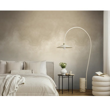 Slaapkamer met licht behang met wolkeneffect, een booglamp, een bed met wit beddengoed en een kleine bijzettafel.