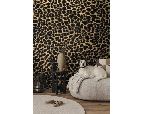 Woonkamer met vliesbehang met luipaardprint, een lichte fauteuil, zwarte bijzetstafel en een decoratieve draadlantaarn.