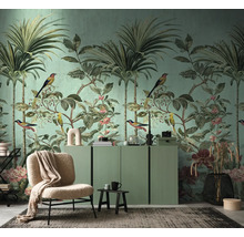 Woonkamer met tropisch behang met palmbomen, vogels en bloemen, een groen dressoir, een beige fauteuil en een vloerkleed.