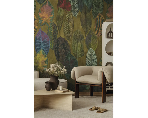 Vliesbehang met groot bladpatroon in natuurtinten in een modern ingerichte woonkamer met een lichte fauteuil en salontafel.
