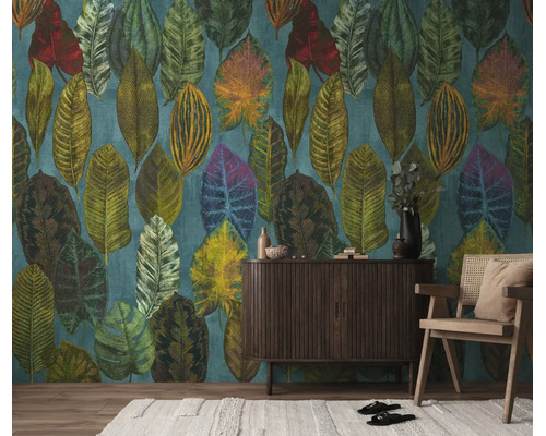 Vliesbehang met groot tropisch bladpatroon in diverse kleuren achter een donker dressoir en een houten stoel.