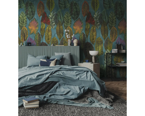 Slaapkamer met behang met grote bladmotieven, bed met geribbeld hoofdbord, blauw beddengoed en een grijs getextureerd tapijt.