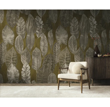 Vliesbehang met groot bladmotief in een woonkamer met houten fauteuil en een dressoir.