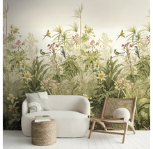 Vliesbehang met botanisch motief van tropische planten, bloemen en vogels, in een lichte kamer met witte bank en houten stoel.