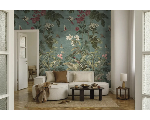 Vliesfotobehang met botanisch patroon, vogels en bloemen in een licht ingerichte woonkamer met een lichte bank en een donkere salontafel.