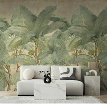 Fotobehang met grote bananenbladeren in een modern ingerichte woonkamer met een lichte bank en marmeren tafel.