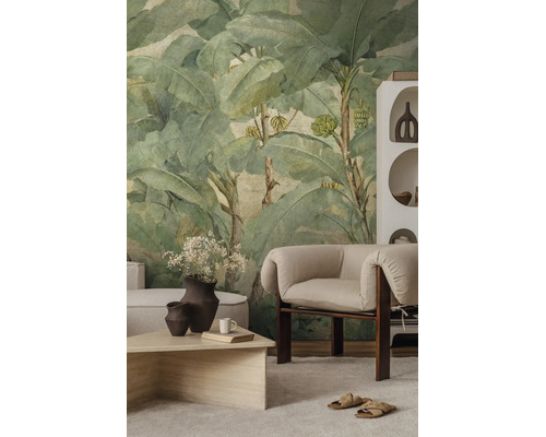 Vliesbehang met bananenbladmotief in vintage stijl in een lichte, modern ingerichte woonkamer met fauteuil en salontafel.