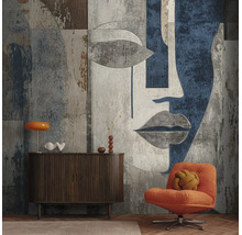 Moderne woonkamerwand met groot formaat fotobehang van een abstract gezicht, donker houten dressoir en oranje fauteuil.