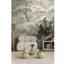 Moderne woonkamer met behang met boommotief, een witte gestoffeerde fauteuil, een glazen salontafel en een driepoot vloerlamp.