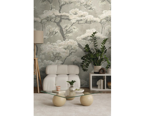 Moderne woonkamer met behang met boommotief, een witte gestoffeerde fauteuil, een glazen salontafel en een driepoot vloerlamp.