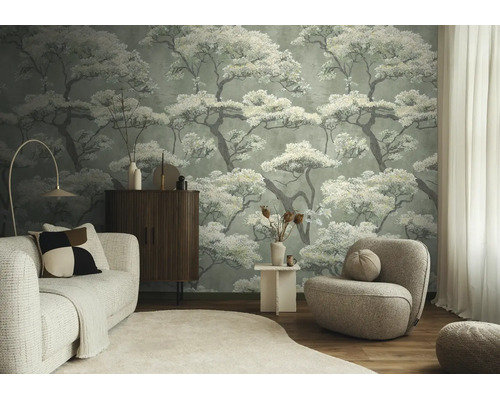 Woonkamer met vliesbehang met boompatroon, lichte bank, donker dressoir en ronde fauteuil.