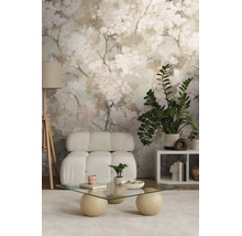 Moderne woonkamer met bloemenbehang, lichte fauteuil, glazen tafel met ronde poten, vloerlamp en kamerplanten op een licht tapijt.