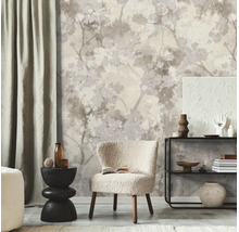 Vliesbehang met bloemrijk takken- en bladerpatroon in neutrale tinten in een modern ingerichte woonkamer met fauteuil en wandplank.