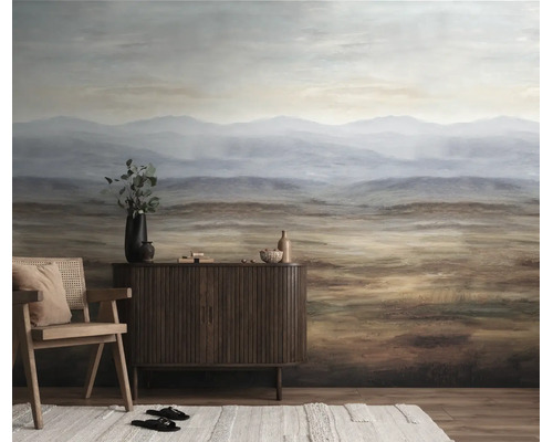 Fotobehang met berglandschap in aardetinten achter een dressoir van donker hout en een fauteuil in de woonkamer.