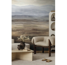 Moderne woonkamer met fotobehang van een abstract berglandschap in aardetinten, beklede fauteuil en een lage houten salontafel.