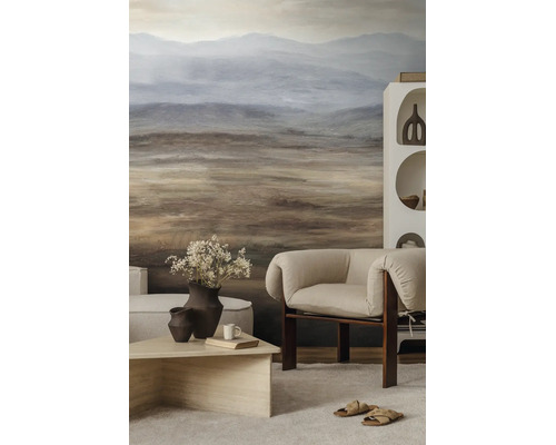 Moderne woonkamer met fotobehang van een abstract berglandschap in aardetinten, beklede fauteuil en een lage houten salontafel.