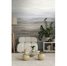 Moderne woonkamer met landschapsfotobehang, witte gecapitonneerde fauteuil, glazen salontafel met bolvormige poten en een houten vloerlamp.