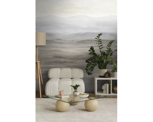Moderne woonkamer met landschapsfotobehang, witte gecapitonneerde fauteuil, glazen salontafel met bolvormige poten en een houten vloerlamp.