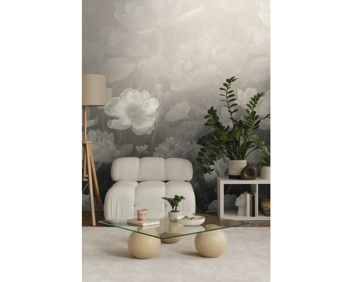 Fotobehang met grote bloemen in grijs en wit in een modern ingerichte woonkamer met een witte fauteuil en een glazen tafel.