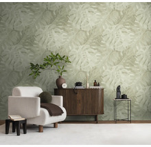 Vliesbehang met groot Monstera-bladpatroon in lichte natuurtint in een modern ingerichte woonkamer met dressoir en witte fauteuil.