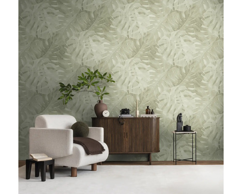 Vliesbehang met groot Monstera-bladpatroon in lichte natuurtint in een modern ingerichte woonkamer met dressoir en witte fauteuil.