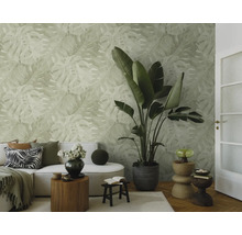 Lichte woonkamer met vliesbehang met monstera-bladmotief, bank, grote kamerplant en decoratieve houten bijtafels.