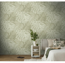 Licht ingerichte slaapkamer met behang met groot monstera-bladpatroon, bed met kussens en een rond nachtkastje.