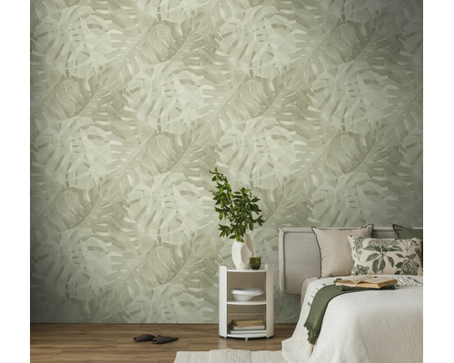 Licht ingerichte slaapkamer met behang met groot monstera-bladpatroon, bed met kussens en een rond nachtkastje.