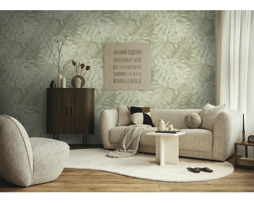 Moderne woonkamer met vliesbehang met monstera-motief, lichtgekleurde bank, donker houten dressoir en organisch gevormd tapijt.