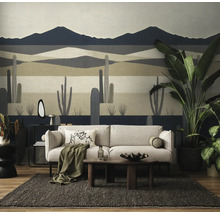 Woonkamer met fotobehang van een woestijnlandschap met cactussen en bergen, met een bank, een houten salontafel en kamerplanten.