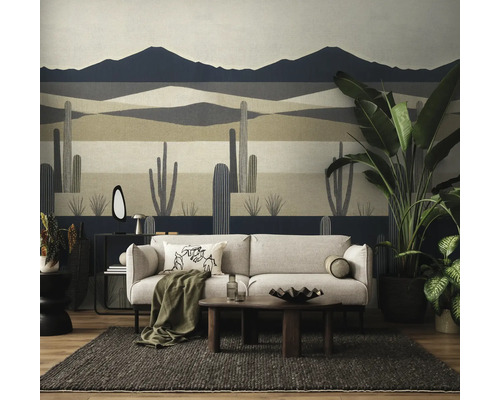 Woonkamer met fotobehang van een woestijnlandschap met cactussen en bergen, met een bank, een houten salontafel en kamerplanten.
