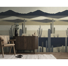 Modern vliesbehang met gestileerd woestijnlandschap, bergen en cactussen in een woonkamer met dressoir en houten stoel.