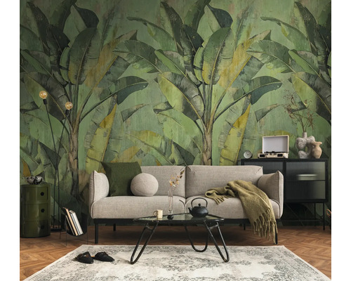 Fotobehang met grote bananenbladeren in vintage-stijl achter een bank in een georganiseerde woonkamer met parketvloer.