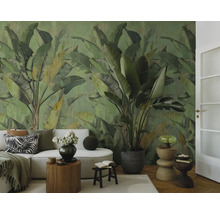 Woonkamer met een groot fotobehang met bananenbladmotief in groentinten, een lichte bank, houten bijzettafels en een grote kamerplant.