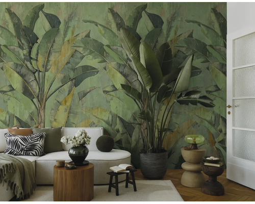 Woonkamer met een groot fotobehang met bananenbladmotief in groentinten, een lichte bank, houten bijzettafels en een grote kamerplant.