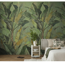 Vliesbehang met een groot bananenbladpatroon in een slaapkamer met een lichte houten vloer en een wit bed.