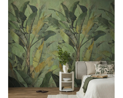 Vliesbehang met een groot bananenbladpatroon in een slaapkamer met een lichte houten vloer en een wit bed.