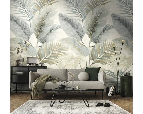 Woonkamer met behang met grote palmbladeren in zachte tinten, grijze bank, zwarte salontafel en vloerkleed op parketvloer.