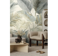 Vliesbehang met grootformaat tropische bladeren in een lichte woonkamer met moderne fauteuil en salontafel.