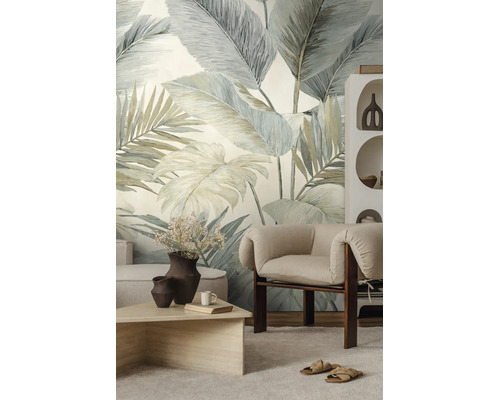 Vliesbehang met grootformaat tropische bladeren in een lichte woonkamer met moderne fauteuil en salontafel.