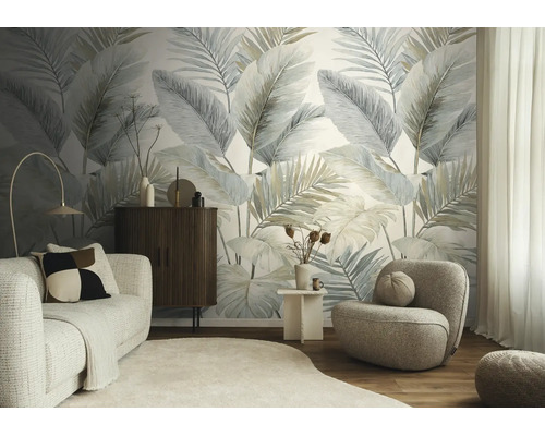 Moderne woonkamer met fotobehang met grote palmbladeren, lichte stoffen bank, donker dressoir en een ronde fauteuil op een houten vloer.