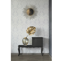 Vliesbehang met damastpatroon op een muur met een ronde zonnespiegel, consoletafel en een vaas met decoratieblad.